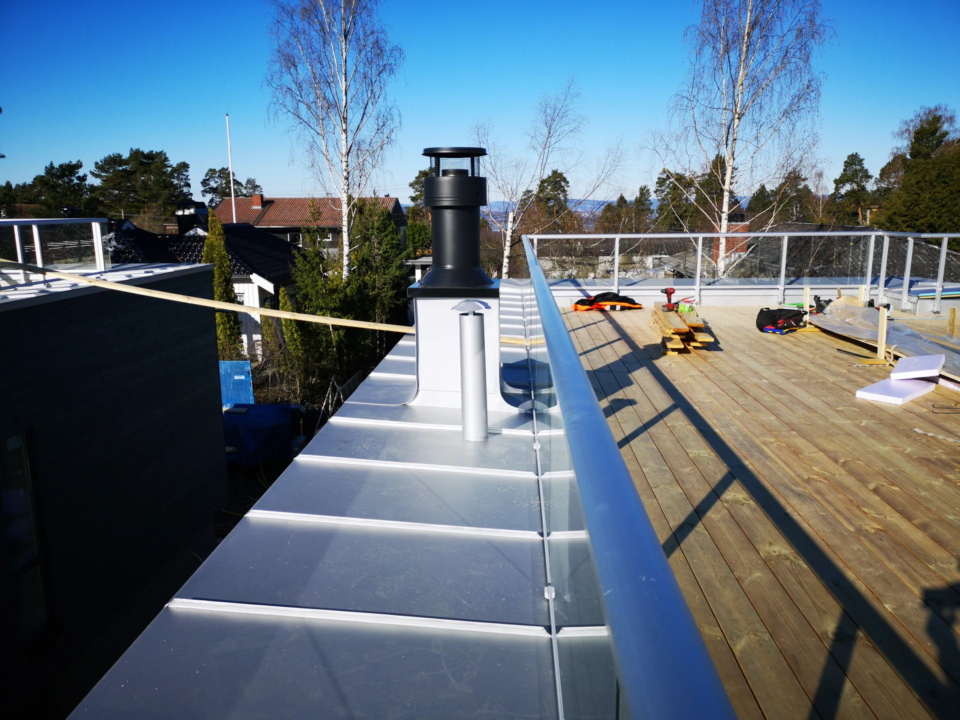 Sølvfarget gesimsbeslag langs takterrasse med glassrekkverk